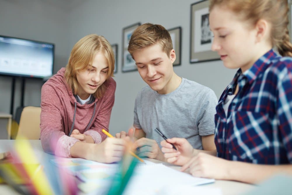 Three teenagers collaborating on homework at a table.