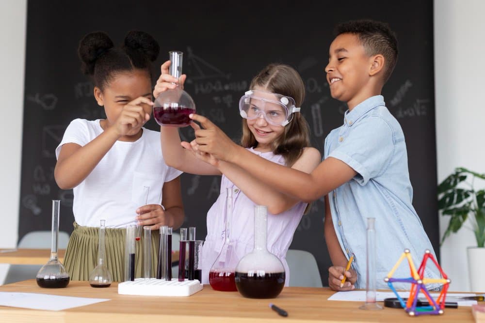 Three children performing a science experiment, examining a flask with a purple liquid; one wears safety goggles.