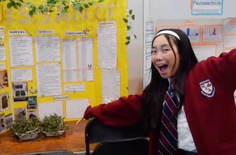 Excited student presenting her science fair project with potted plants.
